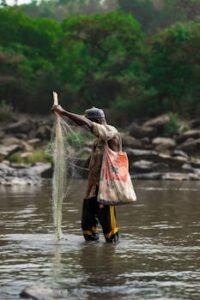 African fisherman with net in Gurara River, Nigeria, showcasing traditional fishing methods.
