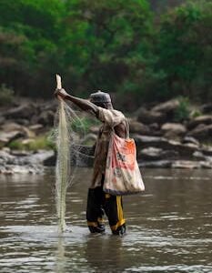 African fisherman with net in Gurara River, Nigeria, showcasing traditional fishing methods.