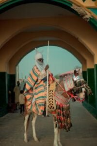 African horseman in colorful attire under an archway, holding a spear.