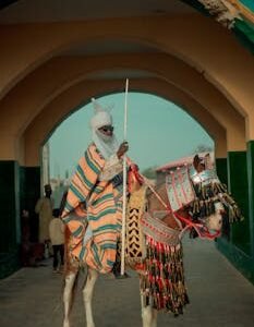 African horseman in colorful attire under an archway, holding a spear.